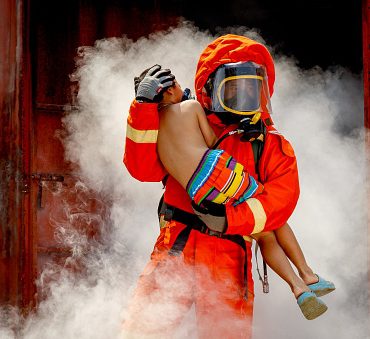 Firefighter, fireman helping injured boy to save him from burning warehouse
